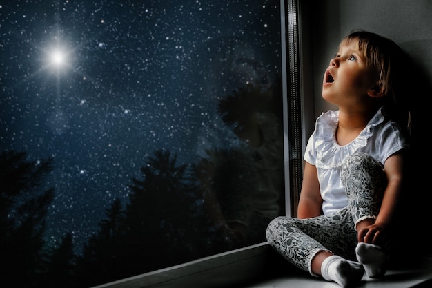 The child looks out the window into the night sky