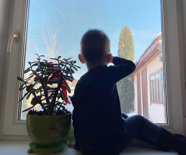 The child looks out the window and waits for parents from work. Selective focus.