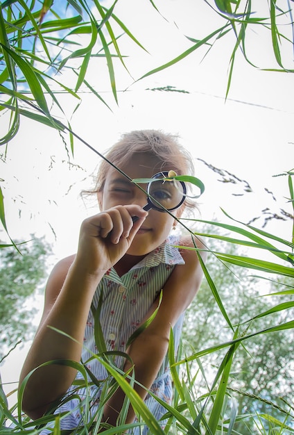 The child looks at the snail through a magnifying glass. Selective focus. Nature.