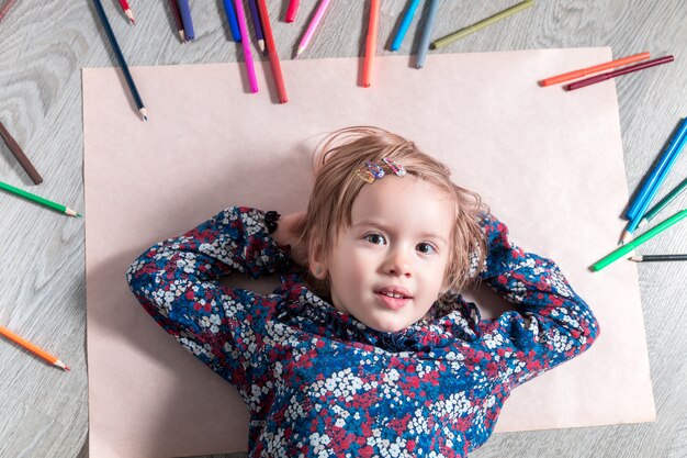 クレヨンの近くの紙の上の床に横たわっている子少女の絵画、創造性の概念の描画