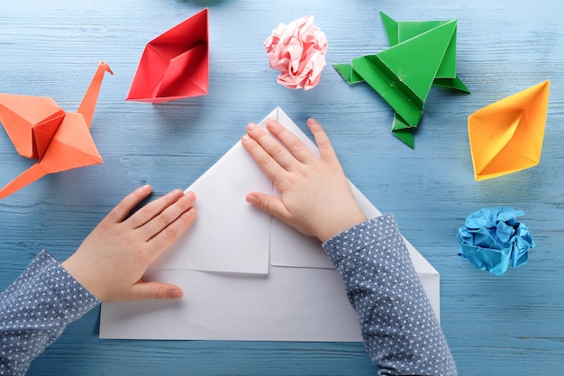 child makes origami on a blue table