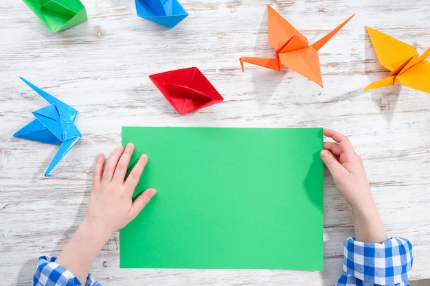 child makes origami from colored paper. Creativity concept.