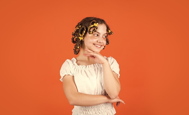 Child making hairstyle little happy girl with curlers in hair fabric mask under eyes for beauty cute kid standing with patches under eyes Child fashion model concept Curled hair with braid