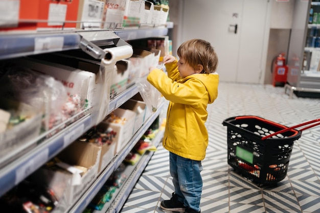 Photo child in the market with a grocery cart puts sweets in a bag