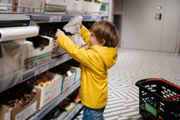 Child in the market with a grocery cart puts sweets in a bag