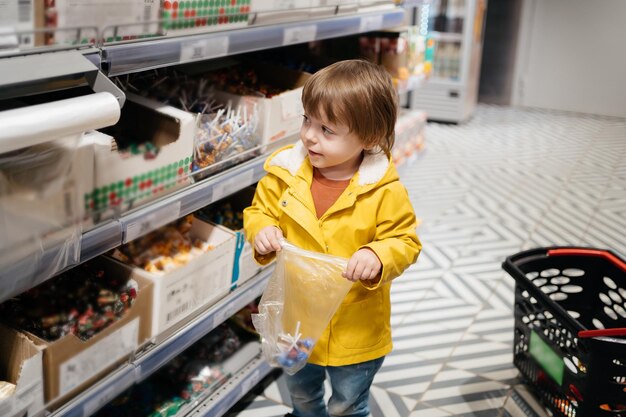 Photo child in the market with a grocery cart puts sweets in a bag