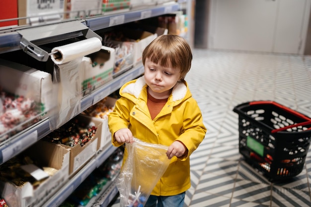 食料品のカートを持っている市場の子供は、お菓子をバッグに入れます