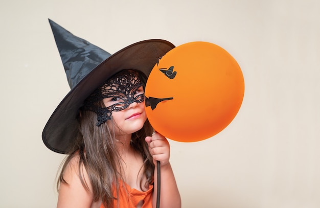 마스크와 모자에 주황색 풍선이 있는 아이. 여자의 할로윈 초상화