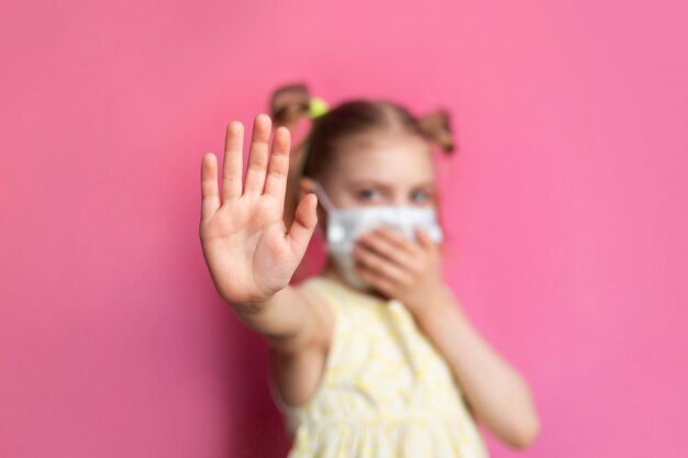 Bambino in una mascherina medica su una parete rosa