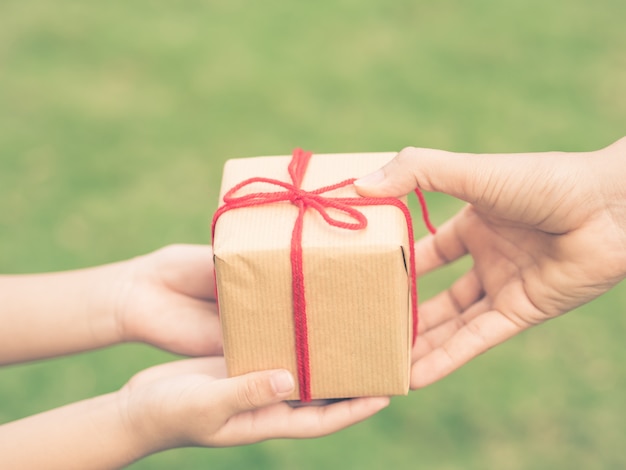 Child and mother hands with gift box over green background. Vintage style.