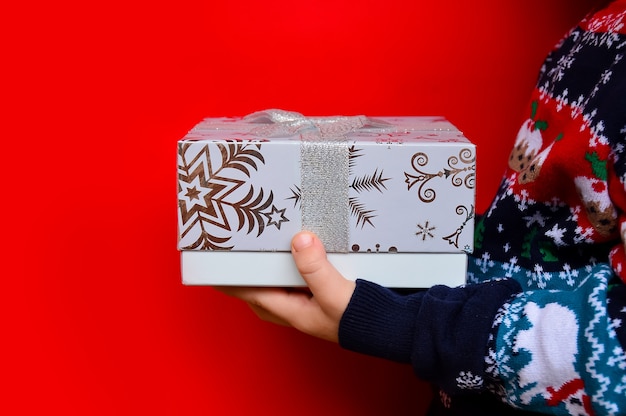 A child in a New Years sweater holds a Christmas gift box on a red background