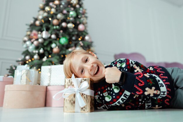 新年のセーターの子供がクリスマスプレゼントに横たわっています