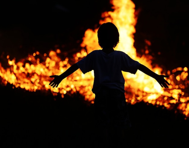 写真 子どもが火の中で大きく開いた腕を持つ