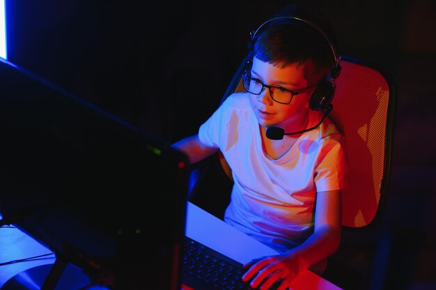 Child online broadcasts computer game, boy streams in\
headphones on rgb lighting background