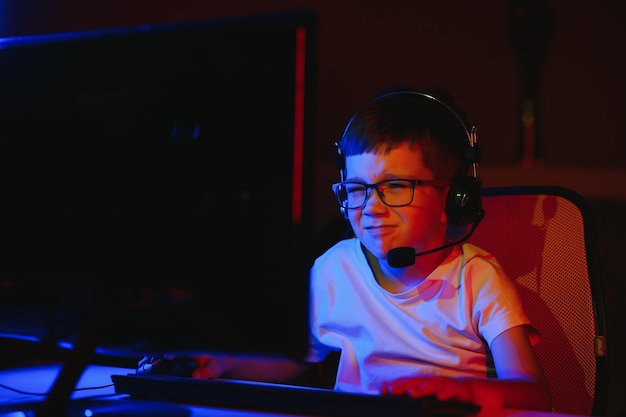 子供がオンラインでコンピューターゲームを放送し、男の子がRGB照明の背景にヘッドフォンでストリーミング