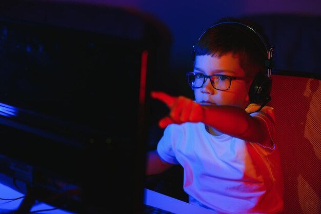 子供がオンラインでコンピューターゲームを放送し、男の子がRGB照明の背景にヘッドフォンでストリーミング