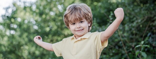 写真 自然の中で屋外の子供幸せな子供緑の木々を背景に隔離された面白い男の子笑顔の子供男の子陽気な陽気な子供手を上げて幸せな子供子供男の子