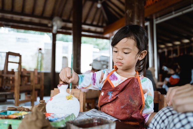 Child painting ceramic pot with paint brush