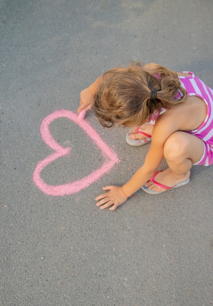 Child paints chalk on the asphalt heart. Selective focus.