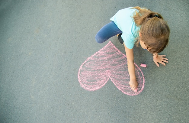 The child paints chalk on the asphalt heart. Selective focus.