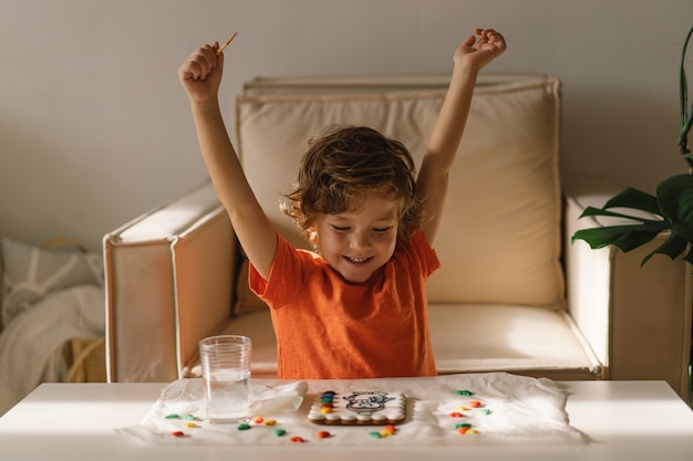 Un bambino dipinge biscotti di pan di zenzero glassati con colorante alimentare