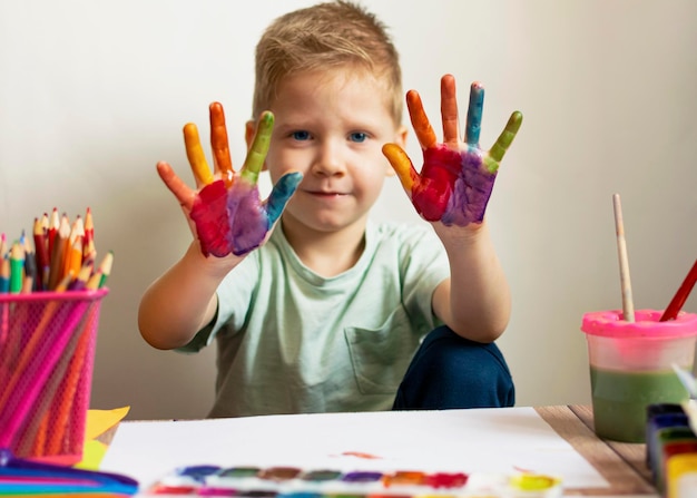 The child paints Palms and hands of a child in multicolored watercolor Watercolor gouache paint brushes colored and wax crayons stickers Set for drawing creativity and hobbies