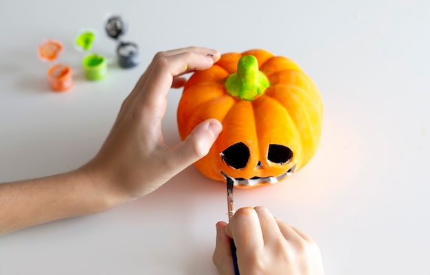 Child paints a pumpkin for Halloween on white background