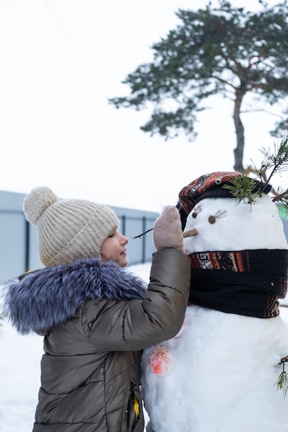 한 아이가 겨울 야외에서 눈사람을 조각하는 겨울 엔터테인먼트와 창의성으로 눈사람의 얼굴을 그립니다.