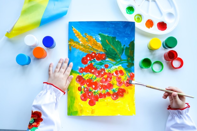 The child paints viburnum symbol and ensign of Ukraine