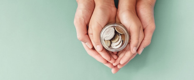 Child and parent hands holding money jar, donation, saving, family finance plan concept