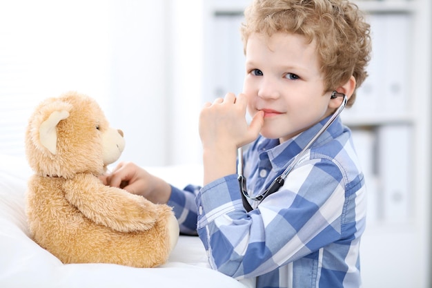 Paziente bambino dopo un esame di salute che gioca come medico con lo stetoscopio e l'orsacchiotto.