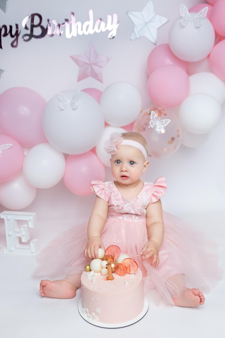 child in a pink dress with a birthday cake on a background of pink air balloons little girls first