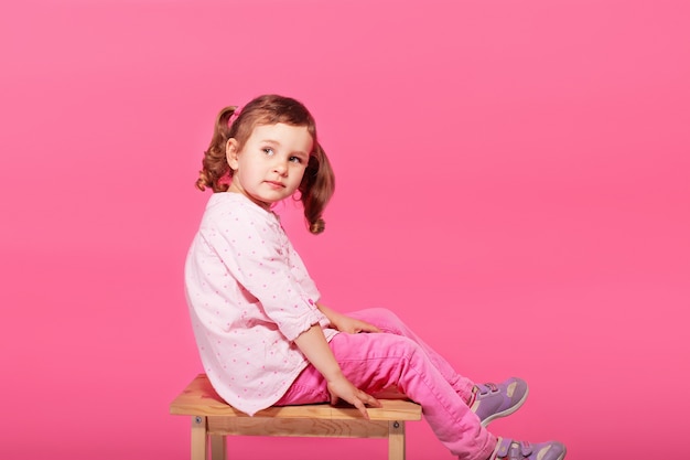 Child playing the ape. Little baby girl wearing pink clothes against a pink