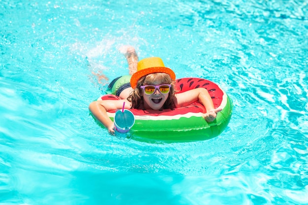 スイミング リングと青い水で遊ぶ子供スイミング プールの子供はリラックスしてインフレータブル リングで泳ぎ、夏休みに水で楽しい時を過す