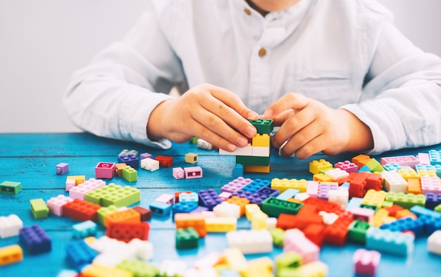 テーブルの上にカラフルなおもちゃのレンガやプラスチックのブロックで遊んで構築している子供。学校または就学前の背景。家庭やクラスでの子供の余暇と教育、早期学習と発達の概念。