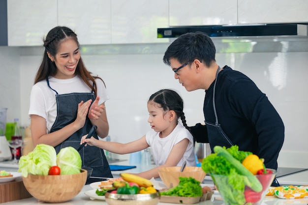 自宅のキッチンで父と母と一緒に料理をする子供がアジアの家族の幸せな瞬間を一緒に