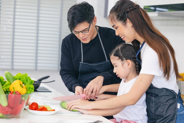 自宅のキッチンで父と母と一緒に料理をする子供がアジアの家族の幸せな瞬間を一緒に