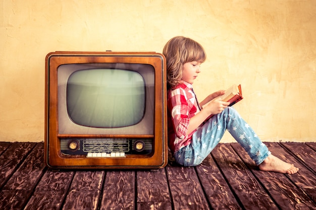 Child playing at home. Kid reading the book near retro TV. Cinema concept