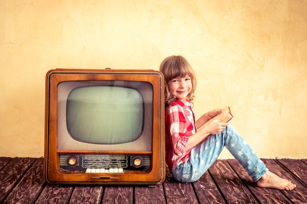 Child playing at home. Kid reading the book near retro TV. Cinema concept