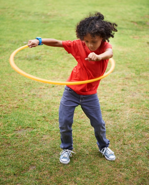 Child playing and hula hoop on field on vacation green grass and sunshine with happiness in city Young boy mexican and game on playground summer holiday and leisure with wellness in urban town