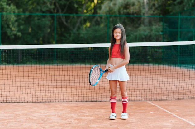 屋外コートでテニスをしている子。テニスラケットとスポーツクラブでボールを持つ少女。子供のためのアクティブな運動