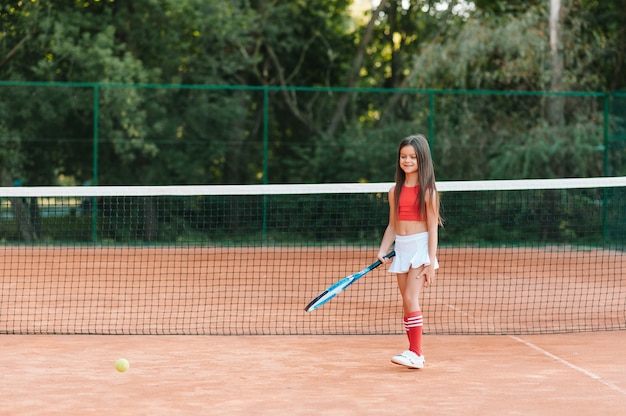 야외 코트에서 테니스를하는 아이. 테니스 라켓과 공 스포츠 클럽에서 어린 소녀. 아이들을위한 활동적인 운동