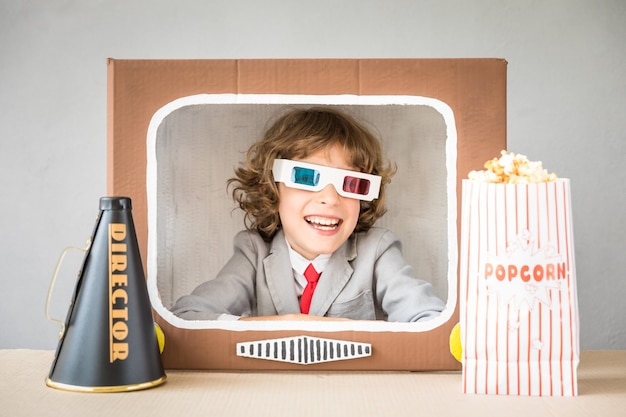 Child playing with cardboard box TV. Kid having fun at home. Video blogging concept