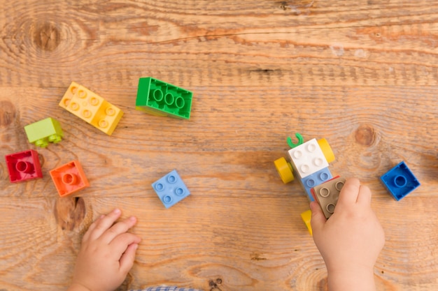 Child playing with colorful toy bricks on wooden background
