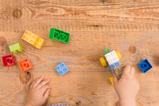 Bambino che gioca con mattoncini giocattolo colorati su fondo in legno