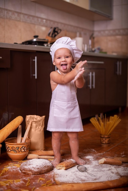 Foto bambino che gioca con la farina in cucina vestito da cuoco