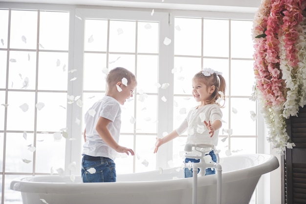 家の浴室で卵の花びらと遊ぶ子供。小さな女の子と男の子が一緒に楽しさと喜びを見せびらかす。幼少期と夢、幻想、想像力の実現