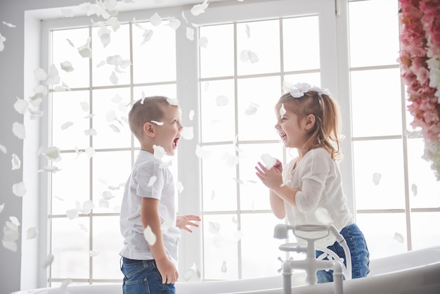 Ребенок играет с лепестками косули в домашней ванной комнате. Маленькая девочка и мальчик fawing веселья и радости вместе. детство и воплощение мечты, фантазии, воображения