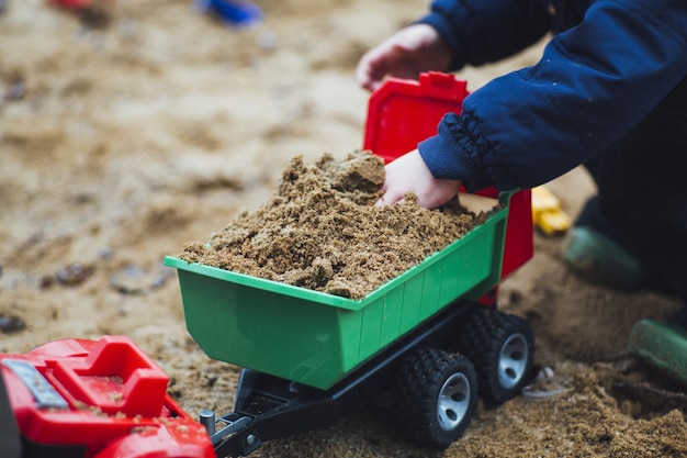 Child playing with sand and plastic toy trucks in a sand box in a park