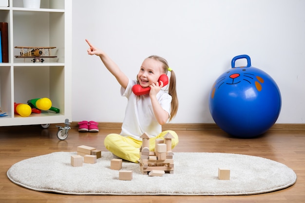ребенок играет в кубики на ковре и разговаривает по телефону